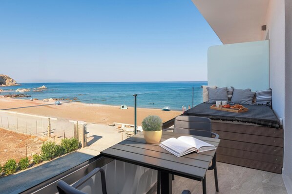 A balcony with a view of the beach, a table with a book and a tray of food, and a potted plant.