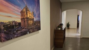 A hallway with a large painting of a historical building, a wooden bench, and a potted plant. - Front Sea View Three bdr Apartment 200 sqm (Tas-Sliema)
