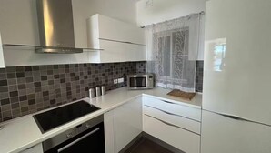 A modern kitchen with white cabinets, a stainless steel range hood, a microwave, and a window with sheer curtains. - Front Sea View Three bdr Apartment 200 sqm (Tas-Sliema)