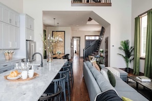 A modern kitchen with grey cabinets, a marble countertop, and a dining area with a grey sofa and wooden dining table. - The 1300 | 2 Designer Homes, Walk to St Charles (New Orleans)