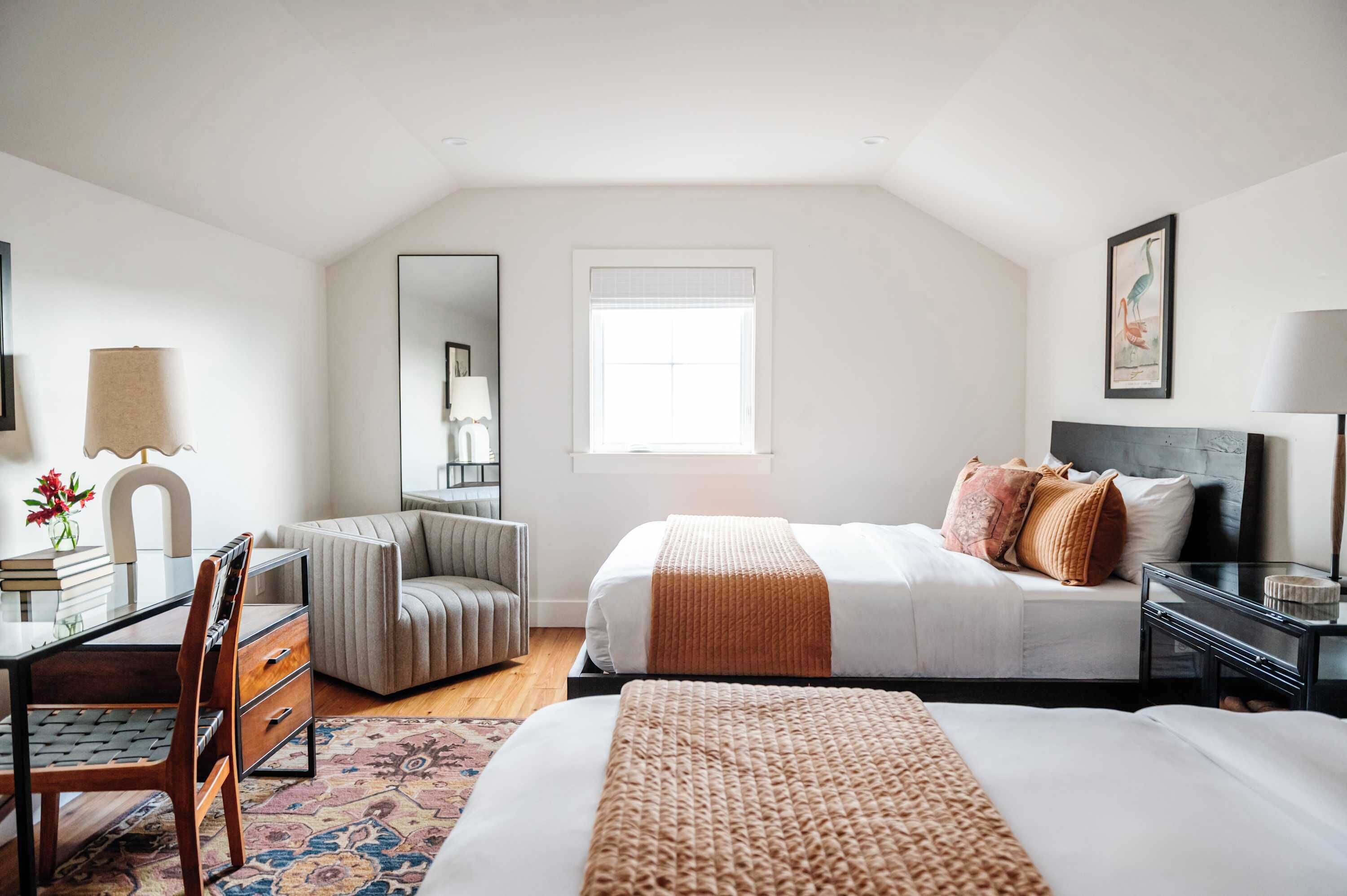 A bedroom with a bed, a desk, a chair, a mirror, and a window.
