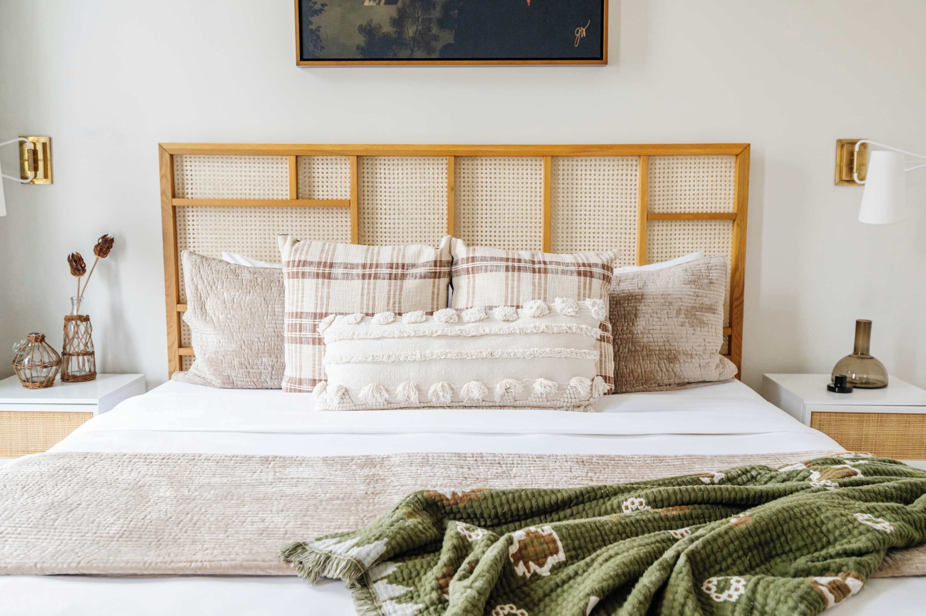 Un letto rifatto con cura, con una testiera in legno, numerosi cuscini e una coperta verde.