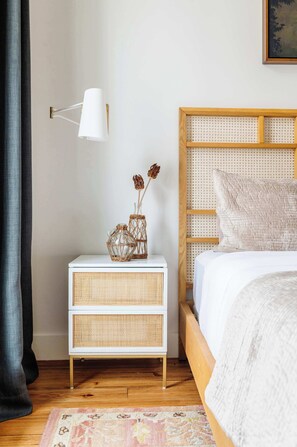 Une chambre avec un lit en bois, des tables de chevet blanches, une lampe fixée au mur et un panier en osier contenant des fleurs séchées.