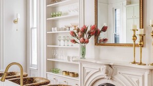 A modern kitchen with a marble countertop, a gold chandelier, and a fireplace with patterned seating. - The Estella | 12-bedroom Suite, Shared Pool (New Orleans)