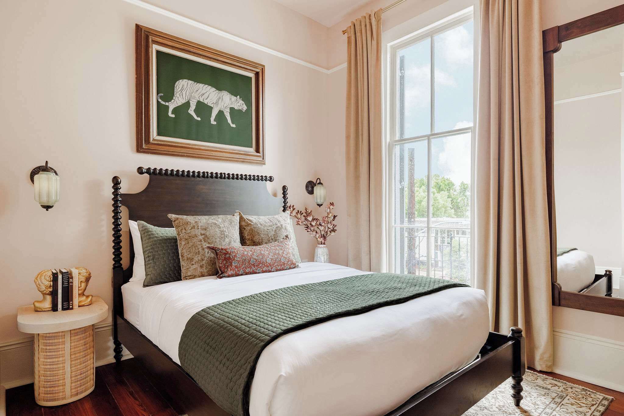 A bedroom with a large bed, a framed picture on the wall, a bedside table, and a window with curtains.