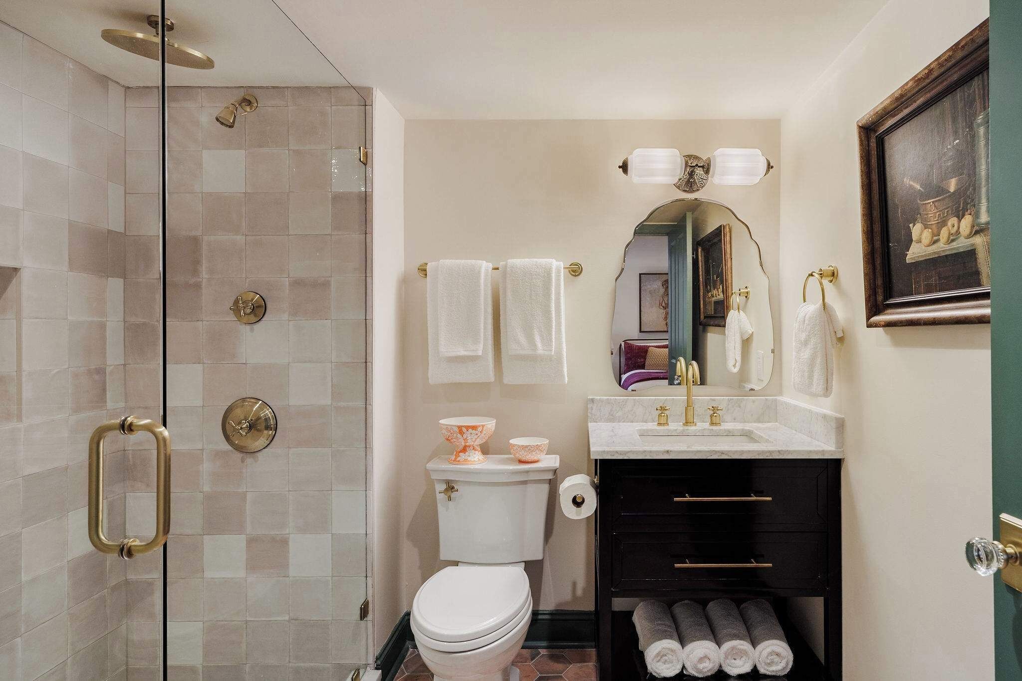 A bathroom with a glass-enclosed shower, a toilet, a sink with a mirror, and a framed picture on the wall.