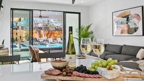 Uma área de refeições com uma tábua de queijos, charcutaria e uvas, uma garrafa de vinho e dois copos de vinho branco.