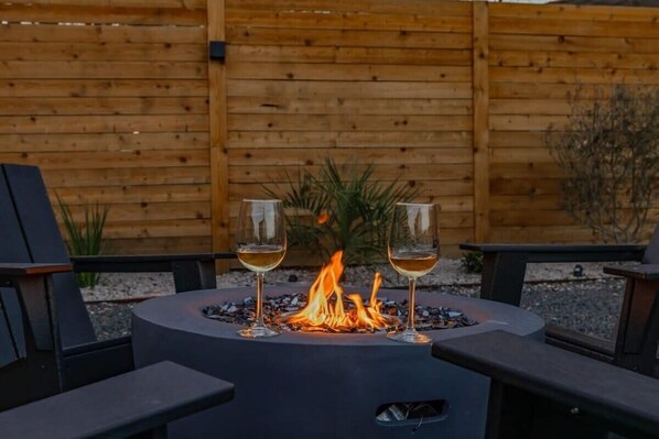 A circular outdoor seating area with a built-in fire pit, two glasses of wine, and a wooden fence in the background.