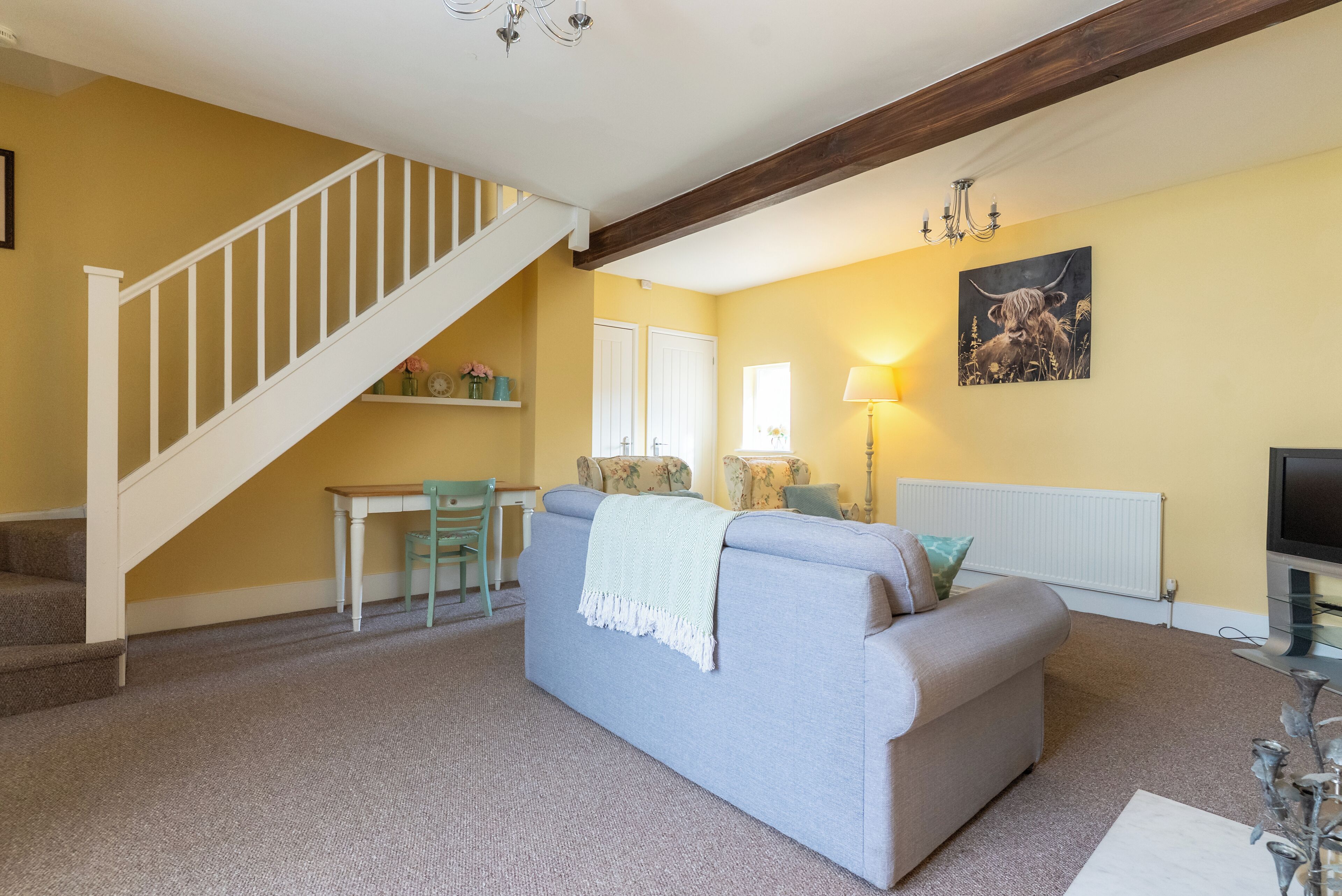A living room with a sofa, a table, a chair, a staircase, and a painting on the wall.