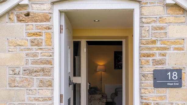 A stone building with a number '18' sign, a wooden door, and a carpeted entrance.
