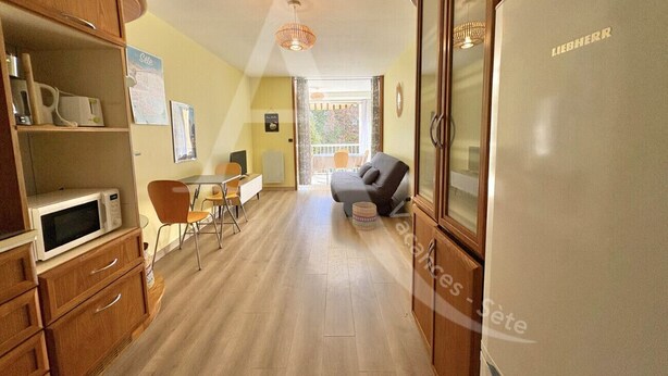 A compact kitchen with wooden cabinets, a microwave, a dining area with a table and chairs, and a refrigerator. - T2 SPACIEUX, LOGGIA ET ACCES WIFI (Sète)