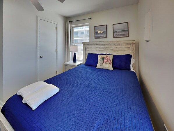 Ein ordentlich bezogenes Bett mit einer blauen Steude, einem weißen Handtuch und zwei Zierkissen.
