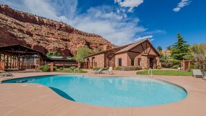 A pool area with a mountain backdrop, a wooden building labeled 'La Estancia', and a stone building nearby.