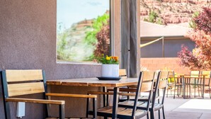 An outdoor patio with wooden tables and chairs, a potted plant with yellow flowers, and a view of red rock formations.