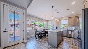 A modern kitchen with a central island, wooden flooring, and a dining area with a table and chairs.