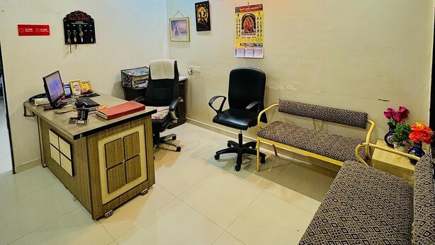 A hotel reception area with a desk, computer, chairs, and a sofa. - Hotel Sai Navsari (Jalalpore)