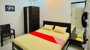 A hotel room with a bed, a wardrobe, a chair, a ceiling fan, and a telephone. - Hotel Sai Navsari (Jalalpore)
