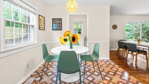 Een eetgedeelte met een ronde tafel, groene stoelen en een vaas zonnebloemen.