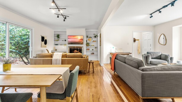 Een ruime woonkamer met een houten eettafel, een grijze bank en een open haard.