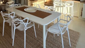 Un soggiorno moderno con zona pranzo, caratterizzato da un tavolo e sedie bianche, un grande specchio e una cucina sullo sfondo.