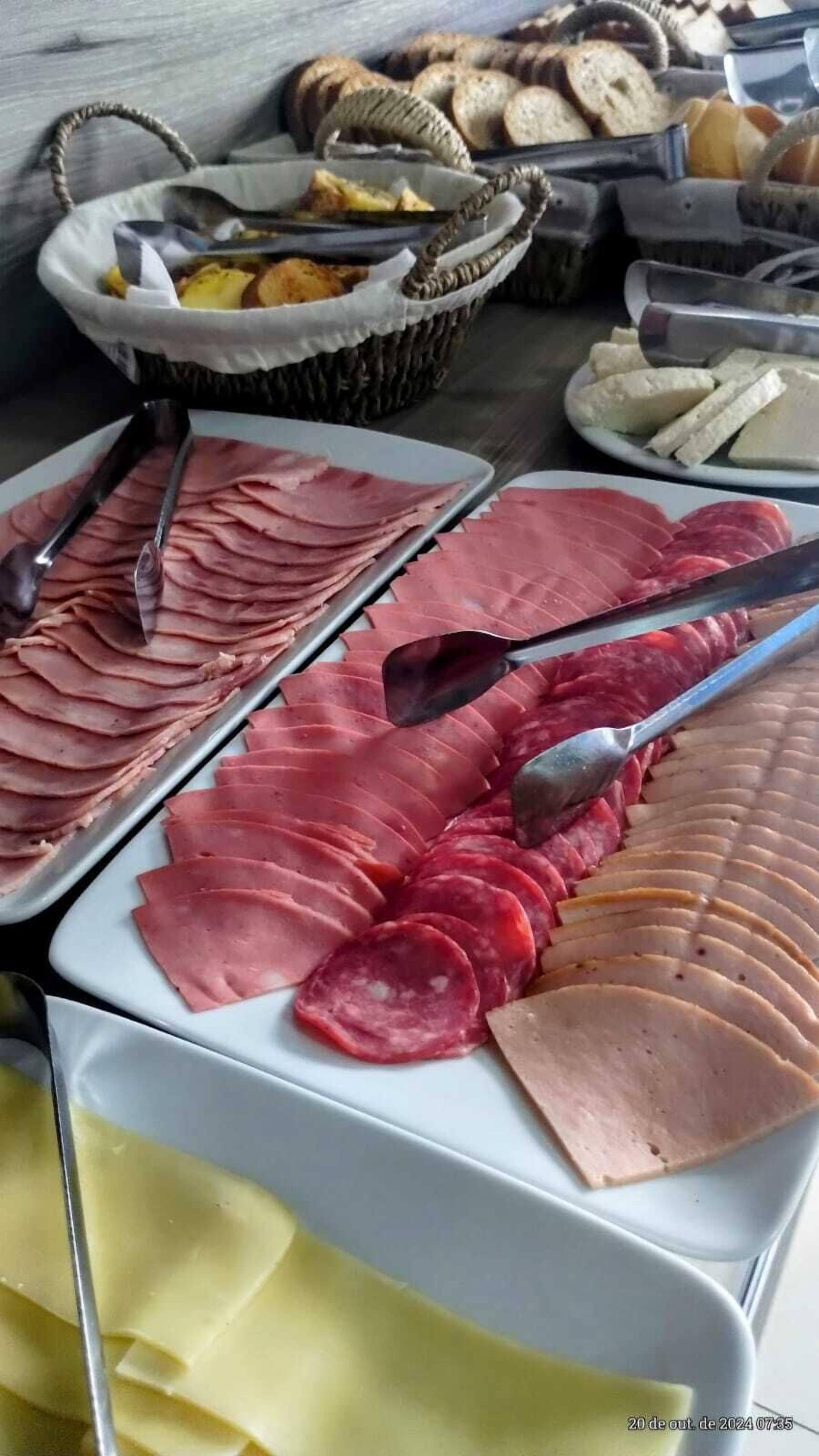Un bufé con varias carnes, incluyendo jamón en rodajas y salami, y una cesta de pan.