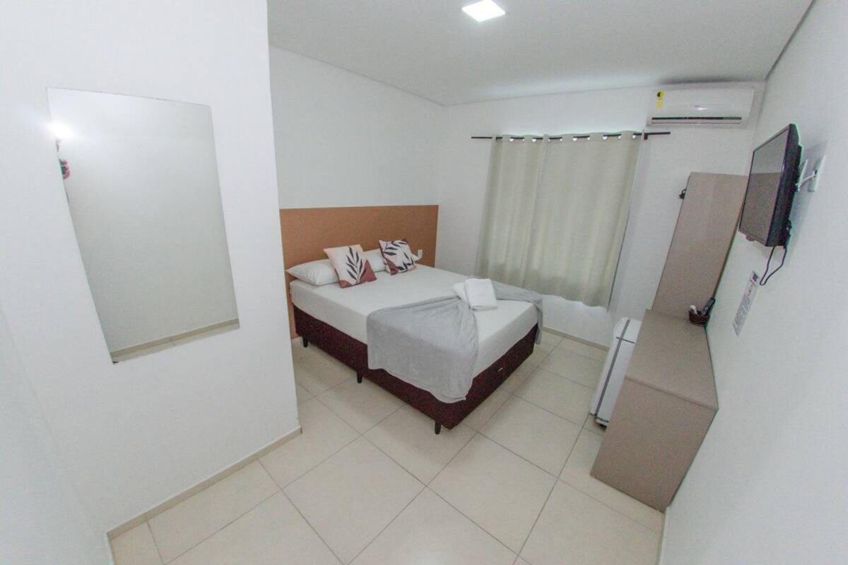 Ein Hotelzimmer mit einem Einzelbett, einem Fernseher, einer Klimaanlage und einem Badezimmer mit Duschvorhang.