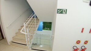 A staircase with a white handrail, a green wall with a fire exit sign, and two fire extinguishers mounted on the wall. - Pousada 4 Estações (Penha)