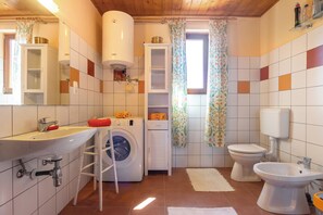 A bathroom with a sink, toilet, bidet, washing machine, and a cabinet. - Lakeside Serenity House (Balatonbereny)