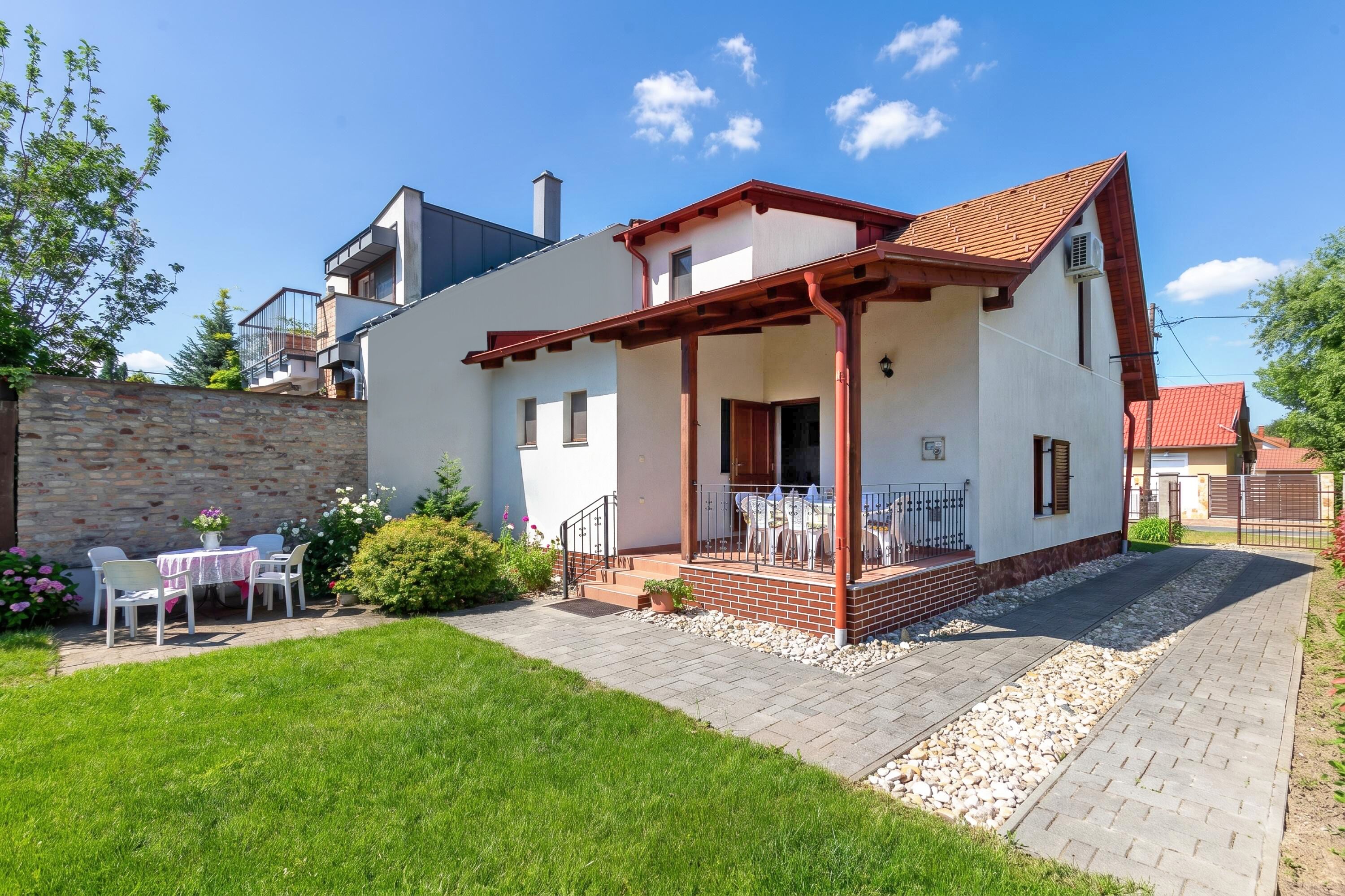 A modern two-story house with a patio, a stone wall, and a garden.