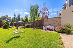A backyard with a lawn, a wooden fence, a brick wall, and outdoor furniture. - Lakeside Serenity House (Balatonbereny)