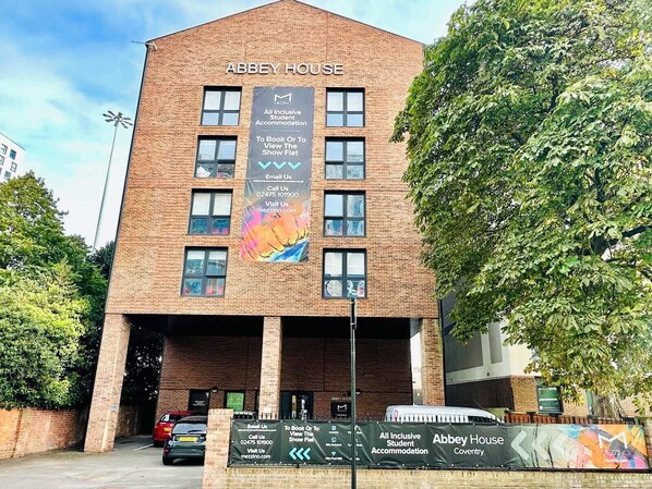 A multi-story brick building labeled "Abbey House" with a sign indicating it offers "All Inclusive Student Accommodation."