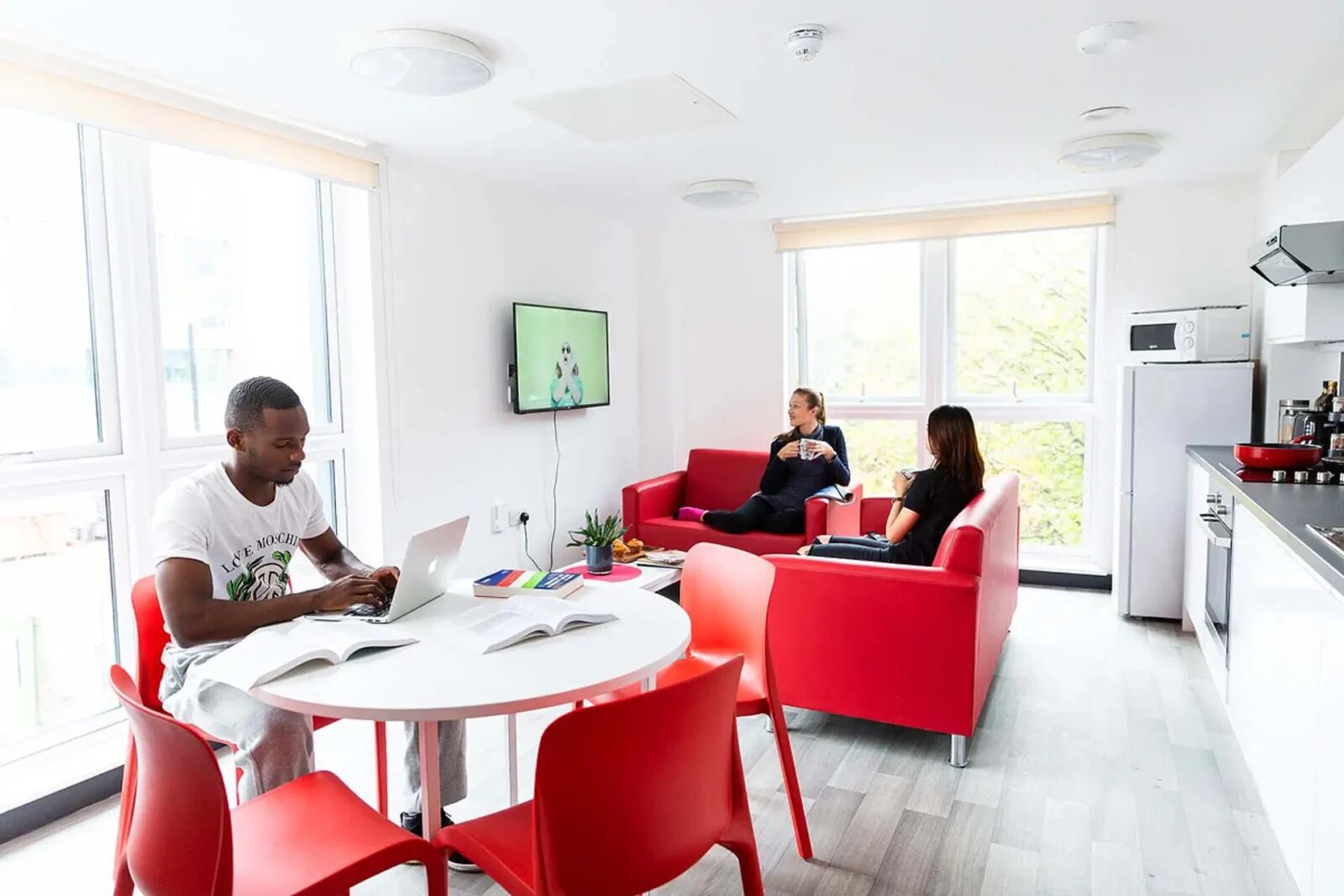 A modern office space with a round table, red chairs, a kitchen area, and large windows.