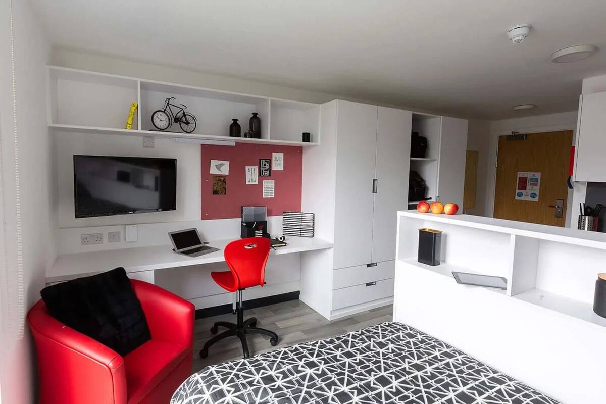 A modern, well-organized room with a red chair, a desk with a laptop, a TV, and various shelves with items.