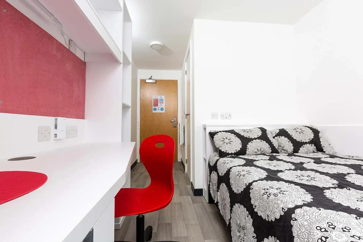 A compact bedroom with a bed, a desk, and a red chair.