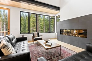 A modern living room with a fireplace, large windows, and a view of trees.