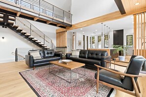 A spacious living area with a black leather sofa, a wooden coffee table, and a patterned rug. A staircase with a metal railing leads to an upper level.