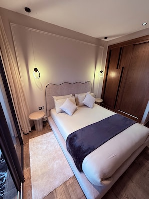 A modern bedroom with a large bed, bedside tables, a wooden wardrobe, and a window with curtains.