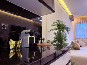 A modern kitchen with a coffee machine, a reflective black countertop, and a potted plant.