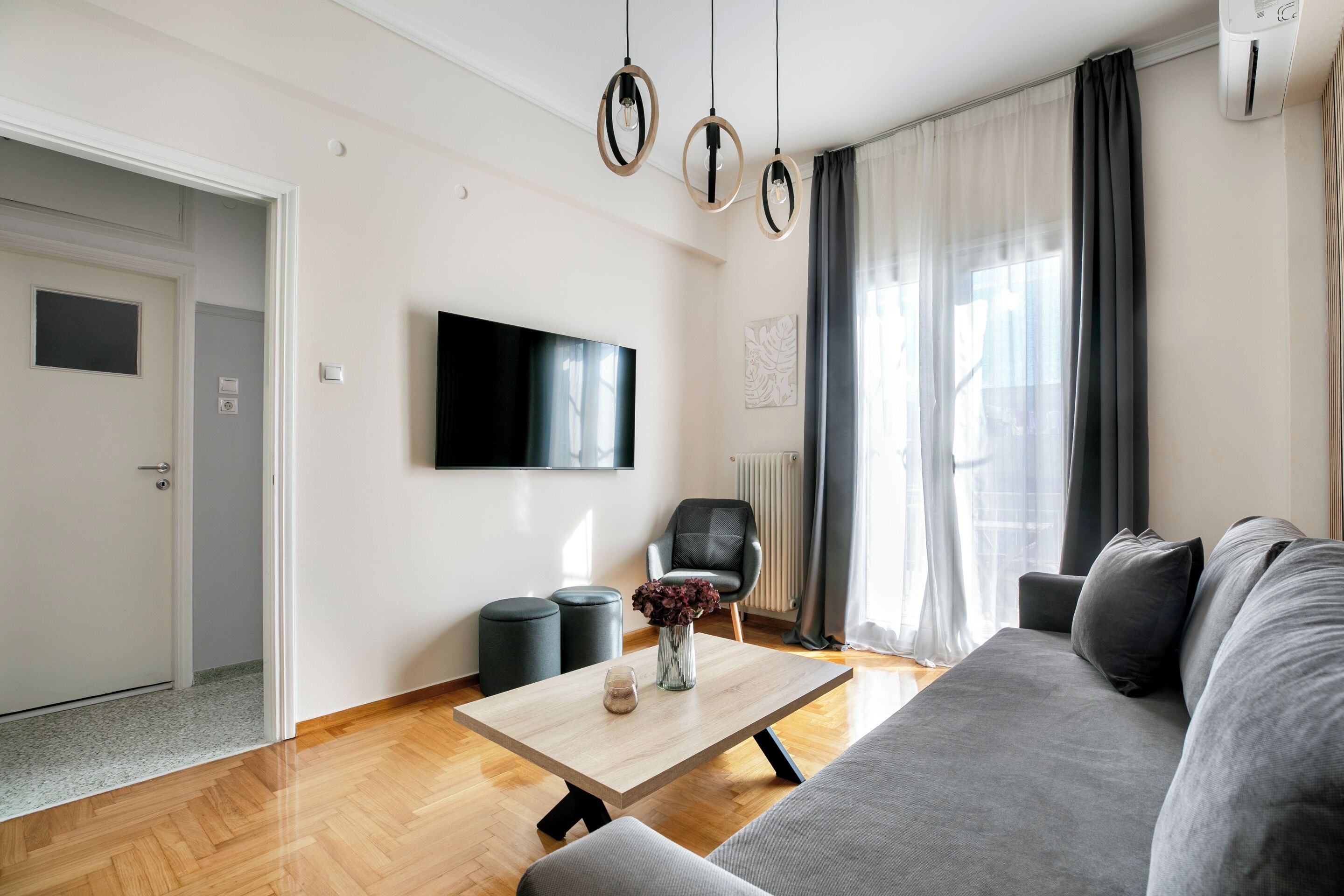 A modern living room with a grey sofa, a wooden coffee table, a flat-screen TV, and a black chair.