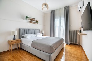 Een moderne slaapkamer met een bed, nachtkastjes, een hanglamp, een radiator en een raam met gordijnen.