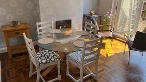 Un coin repas avec une table en verre, des chaises blanches et une petite table d’appoint en bois.