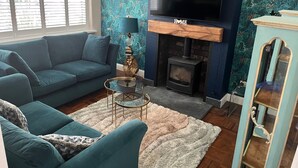 Un salon avec un canapé bleu, un téléviseur, une cheminée et un papier peint à motifs.