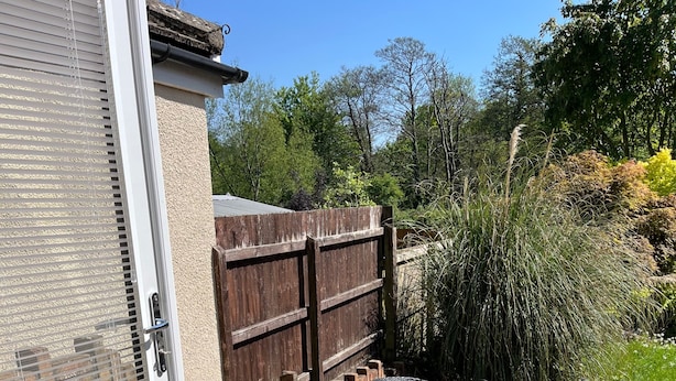 Une terrasse dotée d’une plateforme en bois, d’un chemin en pierre et d’un espace détente avec des meubles en rotin noir.