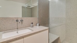 A modern bathroom with a granite countertop, a large mirror, and a shower area. - Urso Tigre Apartment (Funchal)