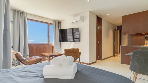 A modern hotel room with a large bed, a desk, a chair, and a TV mounted on the wall. - Urso Tigre Apartment (Funchal)