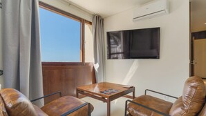 A room with a wooden table and two leather chairs, a flat-screen TV on the wall, and a window with curtains. - Urso Tigre Apartment (Funchal)