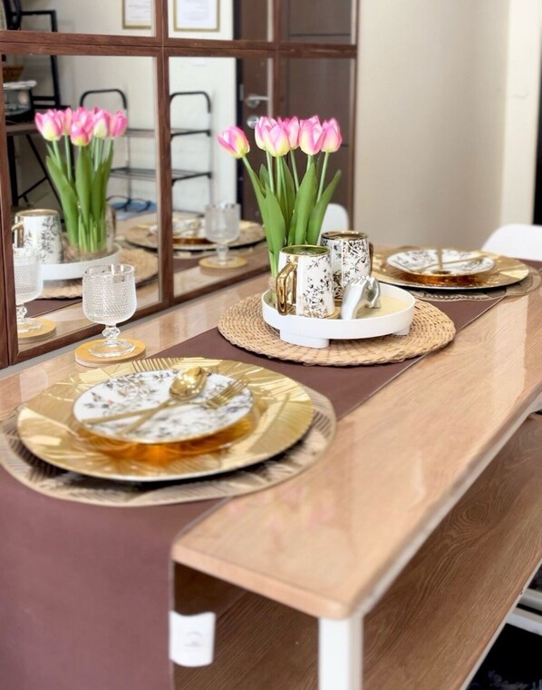 A dining table with a reflective surface, a vase of pink tulips, and a tray with a teapot and cups.