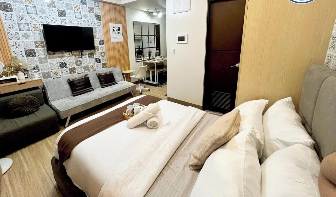 A hotel room with a bed, a sofa, a TV mounted on the wall, and a desk with a chair.