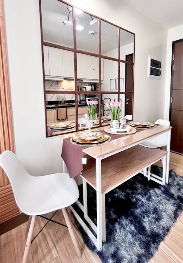 A dining area with a wooden table, white chairs, a mirror, and a kitchen in the background. - Room-the B's Crib Saint Dominique (Iloilo)