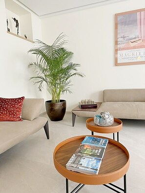 Uma sala de estar com um sofá, uma mesa de centro com revistas, um vaso de planta e um tabuleiro de xadrez.
